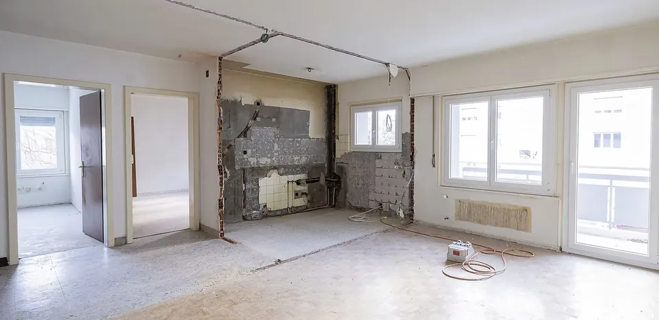Séjour de l'appartement Beaulieu avant travaux : cuisine démontée jusqu'au mur, ouverture sur le séjour en cours, gaines et câbles apparents